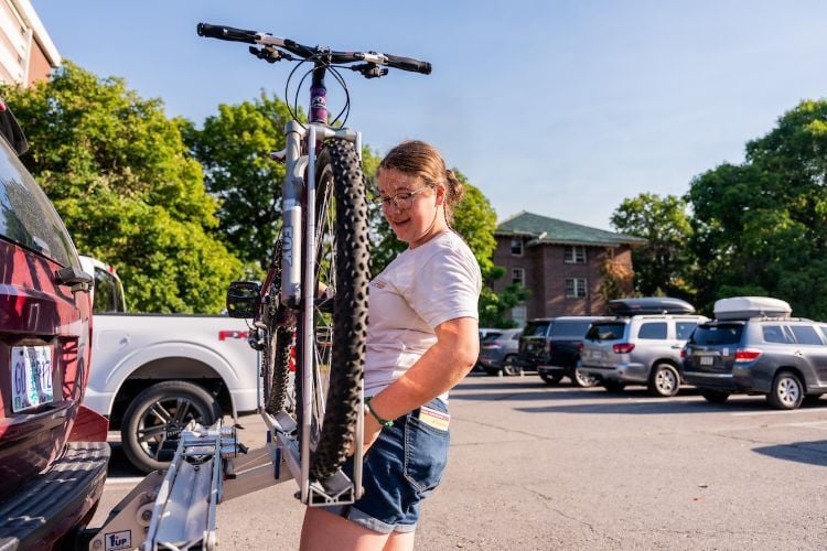 A student loads a bike onto a bike rack on the back of their car