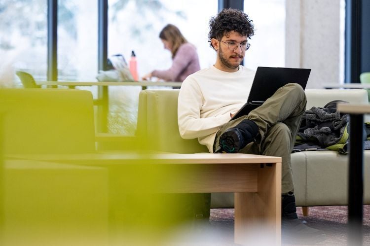 A student sitting on a couch in the library with his computer