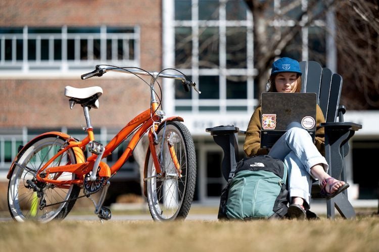 A student sitting on The Oval with a computer