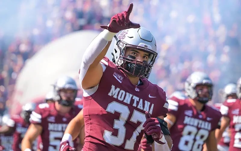 A Griz football player singles No. 1 with his hand as he runs onto the field before a game