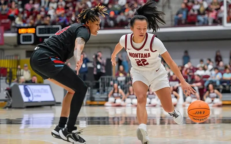 A Lady Griz basketball player dribbles down the court with an opponent guards her