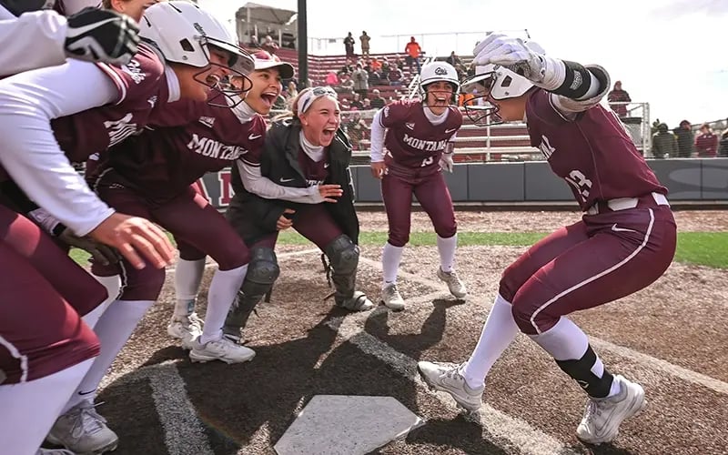 A Griz softball player runs into a huddle of her cheering teammates after hitting a home run