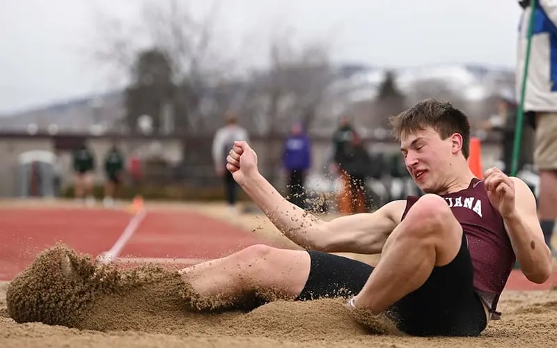 A Griz track athlete lands in the sand after completing the long jump