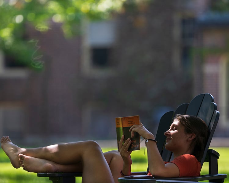 a girl reading franny and zoey in an Adirondack chair on campus