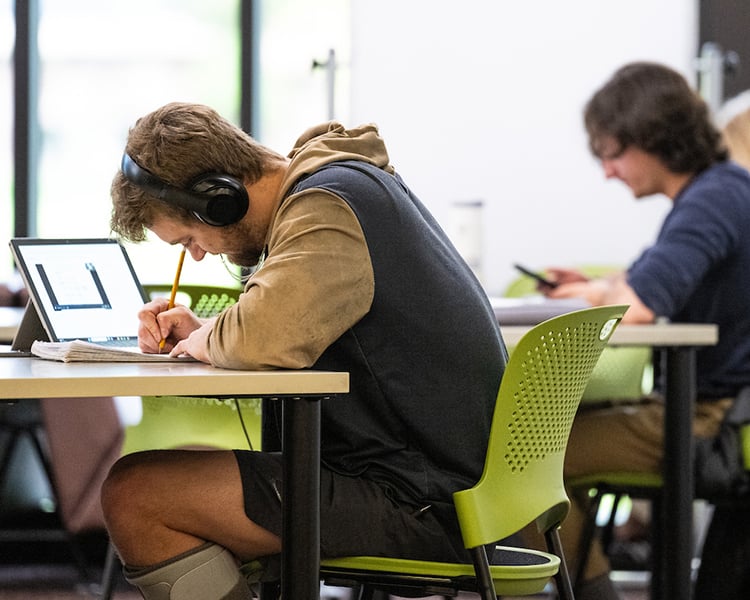 a guy sitting in a chair with his laptop open and he's writing notes