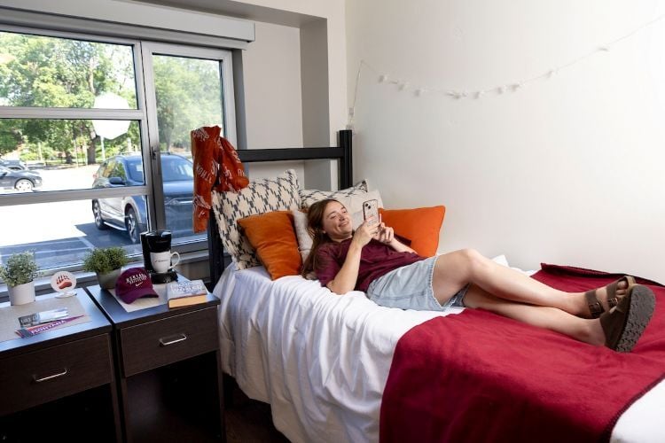 Girl laying on her bed in her dorm playing on phone