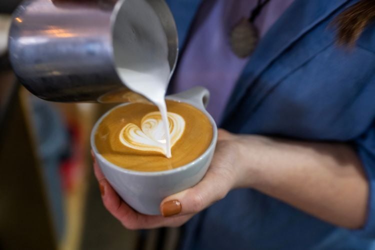 A barista pours cream into a coffee drink