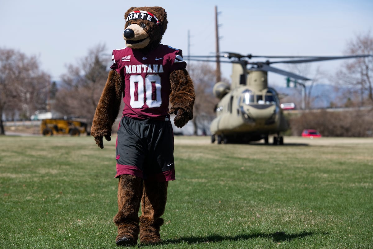 Monte the mascot walking with a military helicopter in the background