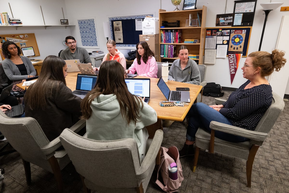 Students and a professor take part in a lab sitting around a table in front of their computers