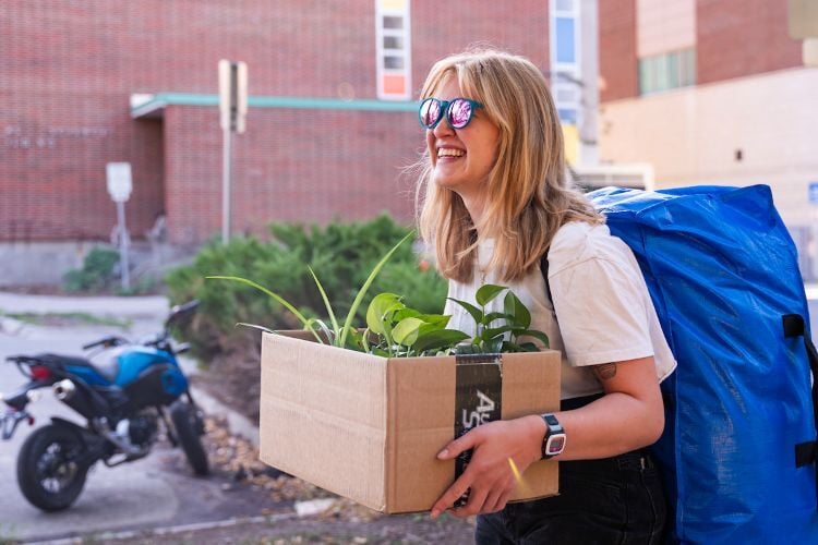 A student carrying a box with plants during move-in