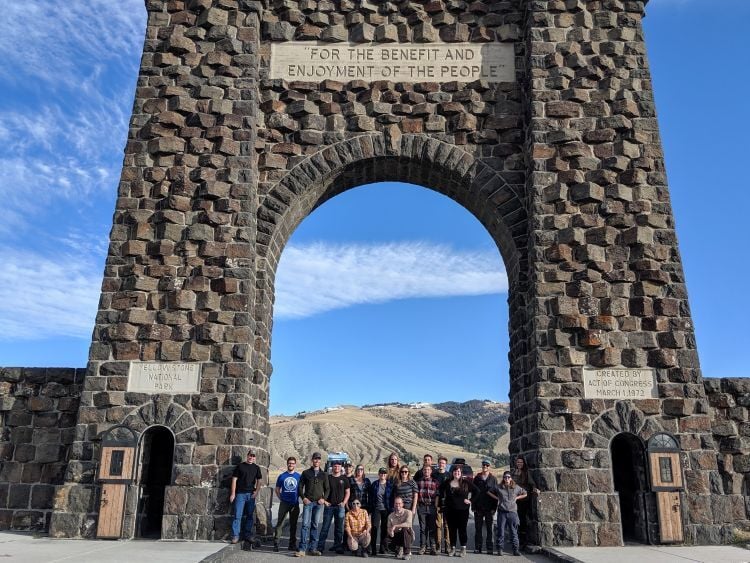 Students in the Parks, Tourism and Recreation Management Program stand below the arched gateway to Yellowstone National Park.