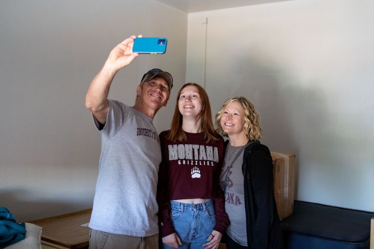 A family takes a selfie in a newly moved-into residence hall