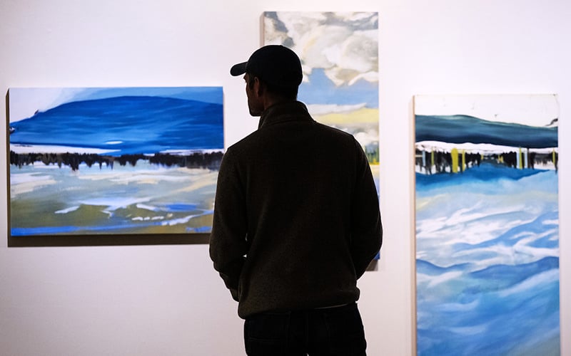 A student attending a gallery opening at UM contemplates the art displayed on the wall