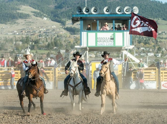 Members of UM Rodeo wave a UM flag while on horses at the fairgrounds