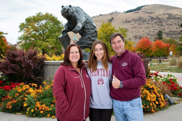 A student and her family standing in front of the Grizzly Statue on campus