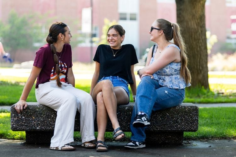 A group of friends sits on a bench outside and chat