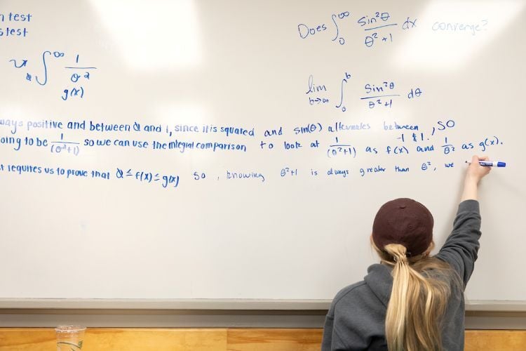 A student writes a long math equation on a whiteboard