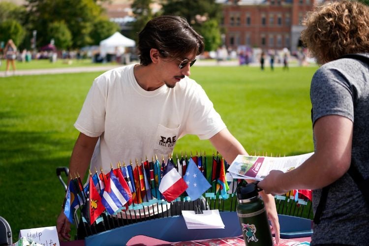 A student stands behind an informational table display with an array of international flags