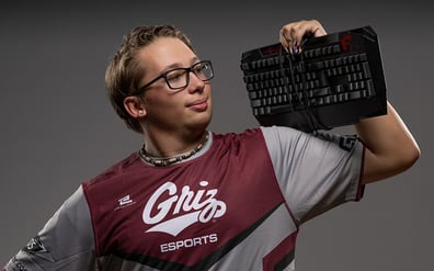 UM student wearing an Esports jersey grips a computer keyboard as he flexes his bicep