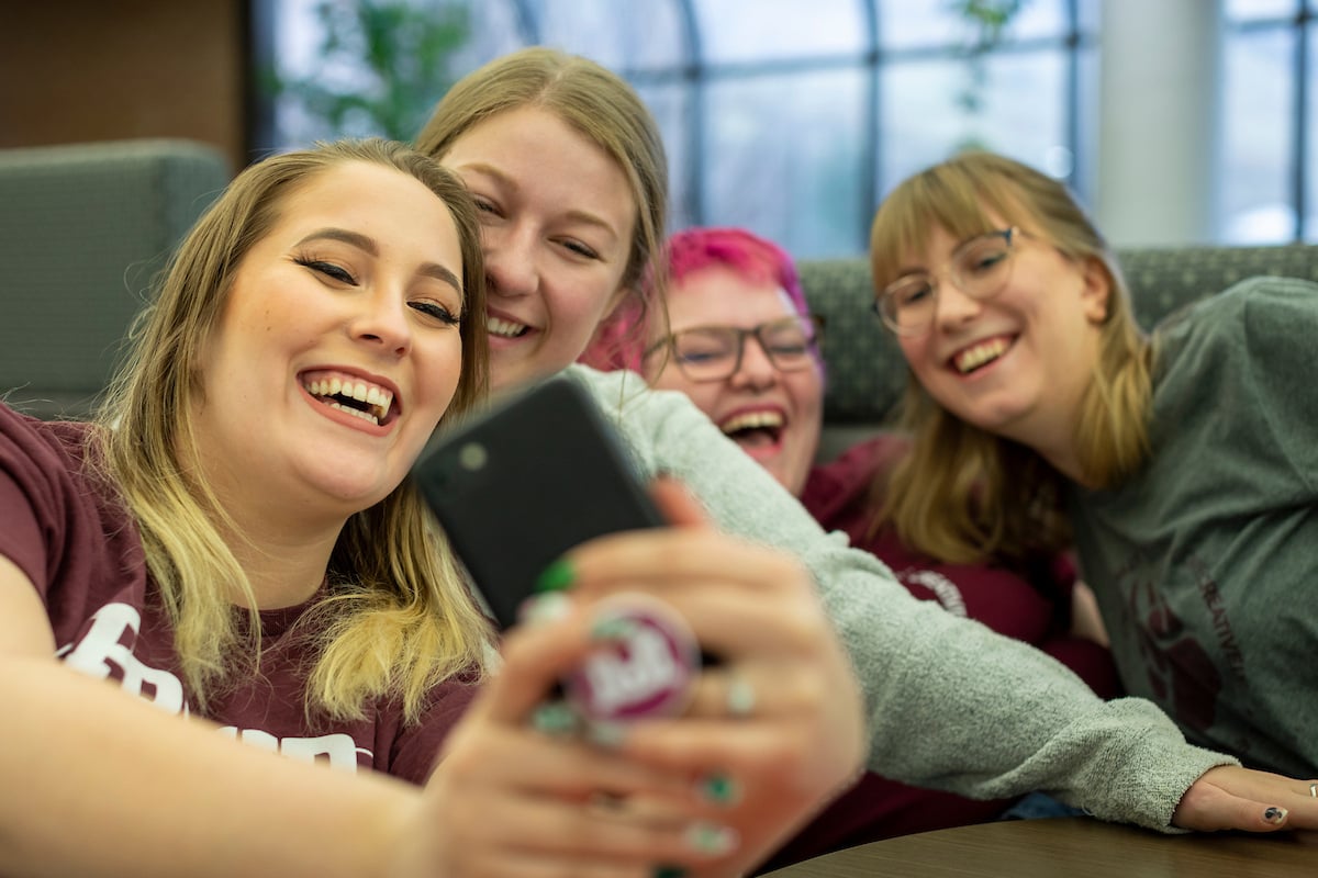 Four friends pose for a selfie in front of a camera